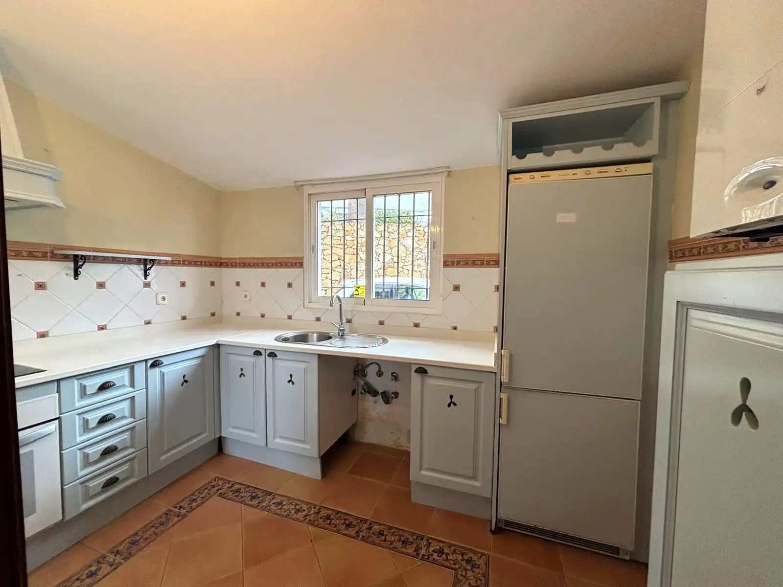 Independent kitchen with exterior window, sink under the window and light-toned cabinetry.