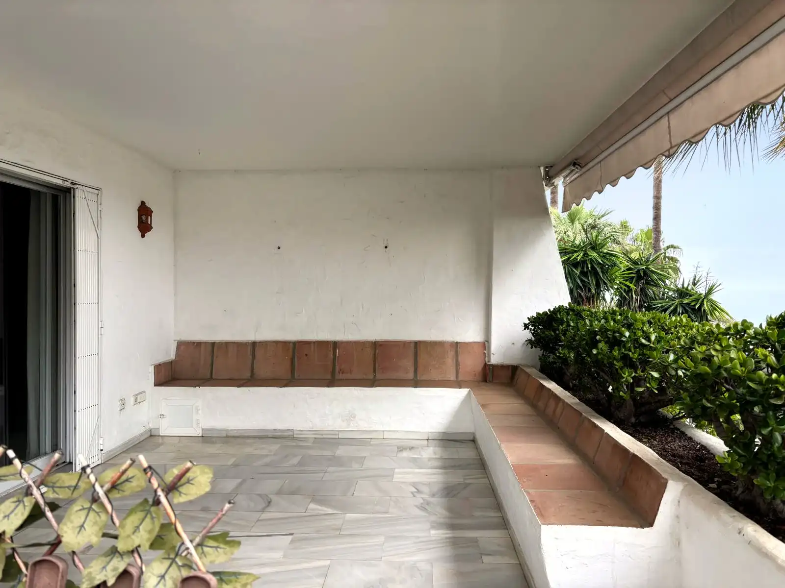 Überdachte Terrasse mit gemauerten Sitzbänken und offenem Blick auf Garten und Bepflanzung in Brisas II, Manilva.